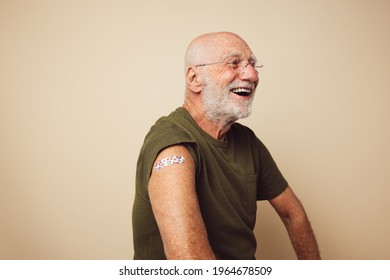 Portrait Of Senior Man With Bandage On Arm After Getting Vaccine. Elderly Man Laughing Against Brown Background After Receiving Immunity Vaccination.