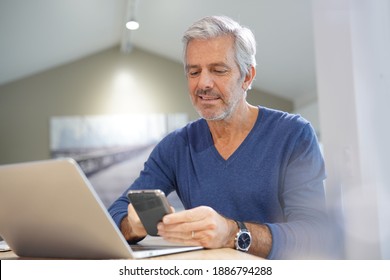 Portrait of senior man with blue shirt using smartphone and laptop