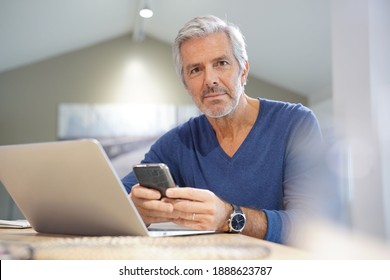 Portrait Of Senior Man With Blue Shirt Using Smartphone And Laptop