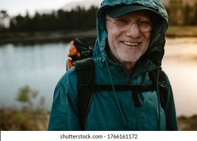 Portrait of a senior man carrying a backpack looking at camera and smiling. Fit old man on a hiking trip with river in background. - Shutterstock ID 1766161172