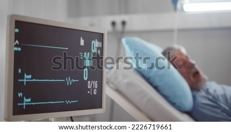 Portrait of senior man in coma dying in hospital bed with heart rate falling on ecg monitor. Aged sick male patient in intensive care unit dead with no heart rate on screen