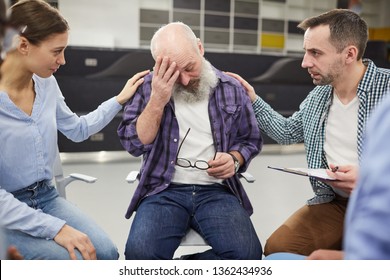 Portrait of senior man crying during group therapy session with two people comforting him, copy space - Powered by Shutterstock