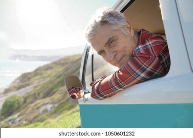 Portrait Of Senior Man Driving Vintage Van By The Ocean