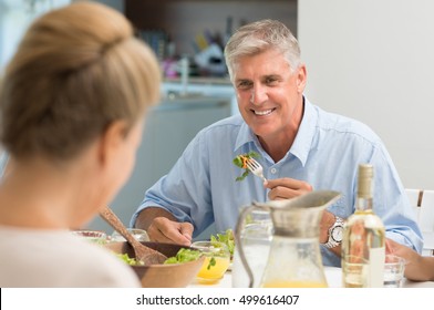 Portrait of senior man eating food while looking at wife. Healthy older man having lunch at home. Cheerful couple enjoying lunch.