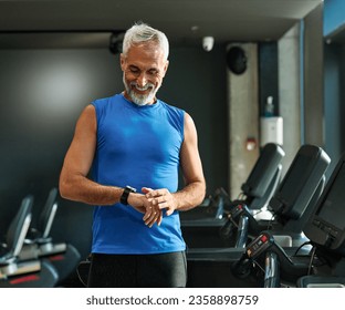 Portrait of a senior man exercising in a gym, mature male running using treadmill machine and checking smart watch for performance, healthy lifestyle and cardio exercise at fitness club concepts - Powered by Shutterstock