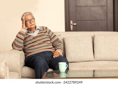 Portrait of senior man feeling disappointed, lost in sad thoughts An elderly man sitting on sofa thinking alone at home - Powered by Shutterstock