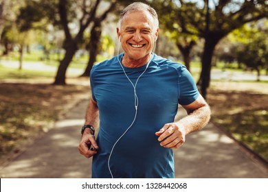Портрет пожилого мужчины в спортивной одежде, бегущего в парке. Закройте улыбающегося человека, бегущего во время прослушивания музыки с помощью наушников.