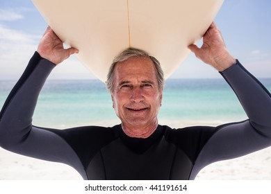 Portrait of senior man holding a surfboard over his head on the beach - Powered by Shutterstock