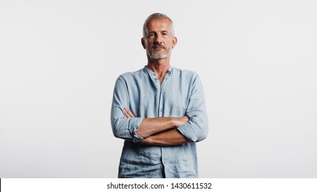 Portrait Of A Senior Man Isolated On White Background. Serious Looking Man Standing With His Arms Crossed Looking At Camera.