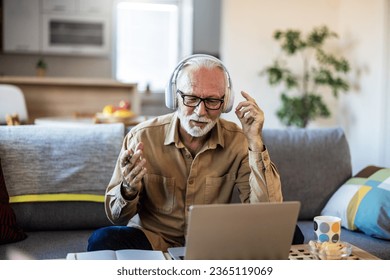Portrait of senior man learning online with headphones and laptop at home, technology and leisure concept. Older mature man using wireless laptop apps browsing internet sit on sofa. - Shutterstock ID 2365119069