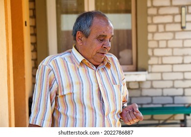 Portrait Of A Senior Man Outdoors. 70s Years Old Latin Or Hispanic Man Standing Outside In Summer Day And Looking Down On His Nails. Casual And Lifestyle Concept.