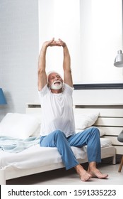 Portrait Of A Senior  Man In Pajamas Waking Up In Bed And Stretching His Arms. Concept Of Energy From The Early Morning Of A Single Retired Man