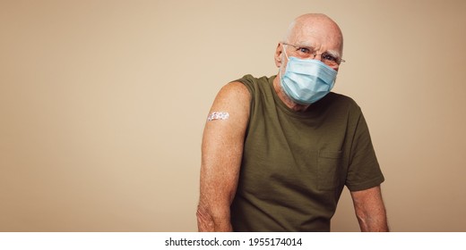 Portrait Of Senior Man With Protective Face Mask Getting Vaccine. Mature Man Against Brown Background After Receiving Corona Virus Vaccination.
