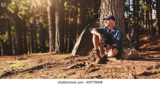 Portrait of senior man sitting by a tree with a tent in background. Mature man sitting at a campsite. - Powered by Shutterstock