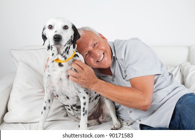 Portrait Of Senior Man Sitting On Sofa With His Pet Dog At Home