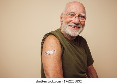 Portrait Of Senior Man Smiling After Getting Vaccine. Mature Man Showing His Arm With Bandage After Receiving Vaccination.