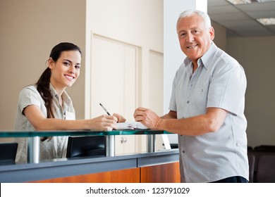 Portrait of senior man standing at hospital reception while female making an entry in book - Powered by Shutterstock