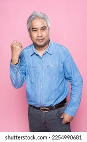 Portrait of senior man standing raising a fist with confident isolated on pink background, Happy elderly man gray hair in a blue shirt. - Shutterstock ID 2254990681