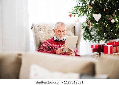 A portrait of senior man with tablet sitting on armchair at home at Christmas time. - Powered by Shutterstock