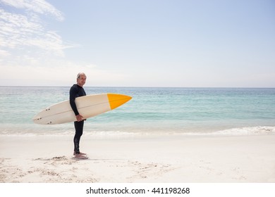 Portrait of senior man in wetsuit holding a surfboard on the beach - Powered by Shutterstock