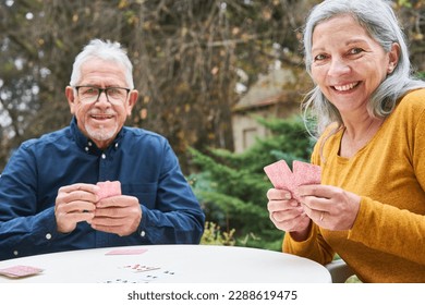 Portrait of senior man and woman playing cards while sitting at table in garden of nursing home