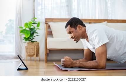 Portrait of senior mature African black man warm up exercise workout yoga plank position at home living room. Yoga for beginner. Guy watching online tutorials on tablet, training, healthy quarantine - Powered by Shutterstock