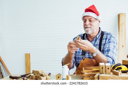 Portrait senior old aging kind Caucasian man or carpenter wearing santa hat, making DIY wooden furniture, holding eyeglasses, smiling with happiness, sitting alone at home. Retirement, Hobby Concept - Powered by Shutterstock