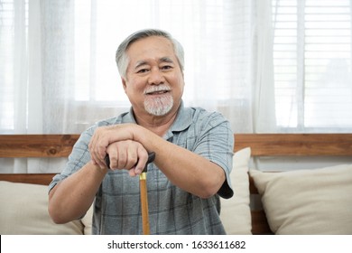 Portrait Of Senior Old Elderly Asian Man Sit On Coach Hand Hold Help Walking Stick Sit On Sofa In House Look At Camera With Happiness And Healthy Lifestyle.