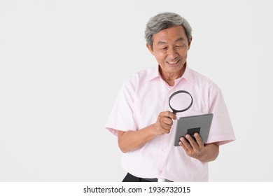 Portrait Of A Senior Older Asian Man Holding And Using Magnifier Glass To See And Watch Screen Of Tablet Computer On White Background. Idea For Older People Eyes Health Problem.