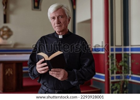 Portrait of senior priest looking at camera while standing with BIble book in church