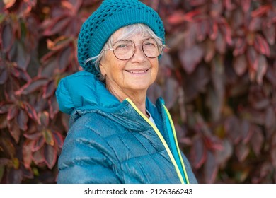 Portrait of senior smiling woman wearing cap and glasses in outdoor walking in a park and looking at camera. Mature attractive caucasian woman enjoying freedom and healthy lifestyle - Powered by Shutterstock