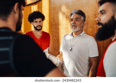 Portrait of a senior trainer standing with his multicultural team and talking after training at indoor court. A professional old coach is standing with his interracial team and discussing training. - Powered by Shutterstock