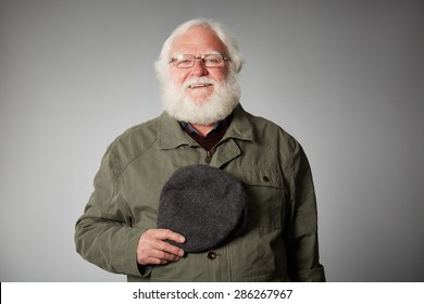 Portrait Of Senior War Veteran Looking At The Camera Wearing Coat And Holding A Cap Against Grey Background