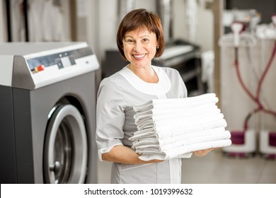 Portrait of a senior washwoman in uniform standing with towels in the hotel laundry