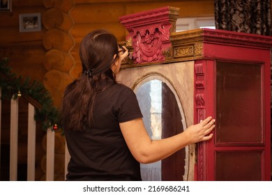 Portrait Of Senior Woman Coloring Shabby Cupboard With Good-looking Carved Ornaments In Red Color With Brush. Reuse Of Old. Workshop For Old Antique Furniture Restoration At Home. Eco-friendly.