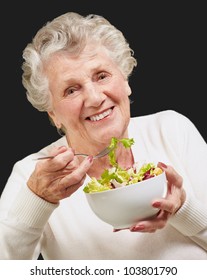 Portrait Of A Senior Woman Eating A Fresh Salad Over A Black Background