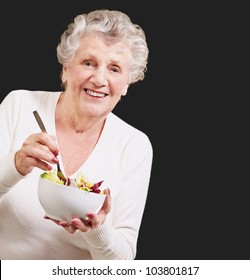 Portrait Of A Senior Woman Eating A Salad Over A Black Background