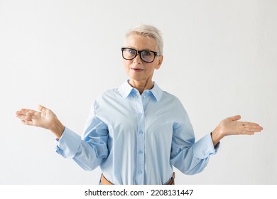 Portrait Of Senior Woman Expressing Surprise. Female Model In Blue Shirt Spreading Arms In Amazement. Portrait, Studio Shot, Surprise Concept