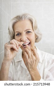 Portrait Of Senior Woman Flossing Teeth In Bathroom