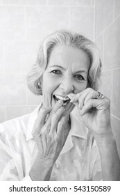 Portrait Of Senior Woman Flossing Teeth In Bathroom