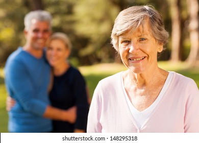 portrait of senior woman in front of middle aged son and daughter-in-law outdoors
