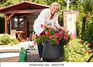 Portrait Of Senior Woman Gardening At Home. Retired Female Cares Of Plants While Standing In Her Beautiful Garden.