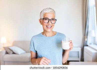 Portrait Of A Senior Woman With A Glass Of Milk. Beautiful Elderly Woman In Grey T-shirt With A Glass Of Milk. Senior Woman Drinking Milk At Home