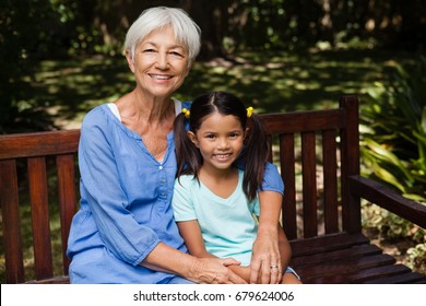 Portrait of senior woman with granddaughter sitting on wooden bench at backyard - Powered by Shutterstock