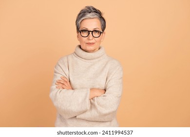 Portrait of senior woman gray haired in stylish warm turtleneck folded arms confident market researcher isolated on beige color background