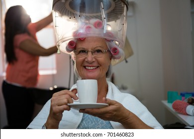 Portrait of senior woman having drink while sitting under hair steamer in salon - Powered by Shutterstock