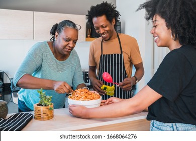 Portrait Of Senior Woman Helping Daughter And Son In Law To Cook At Home. Family And Lifestyle Concept.