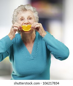 Portrait Of A Senior Woman Holding An Orange Slice In Front Of Her Mouth, Indoor