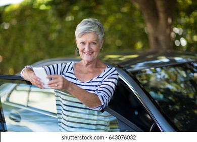 Portrait of senior woman holding phone while leaning on car door - Powered by Shutterstock