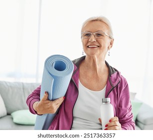 Portrait of a senior woman holding water bottle and exercise mat smiling and posing at home healthy living - Powered by Shutterstock